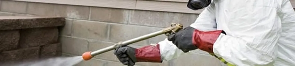 Pest control technician applying exterior insect treatment along a home foundation in Glendale, AZ