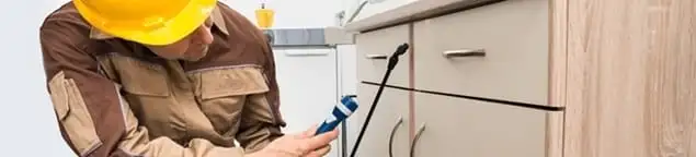 Roach exterminator applying treatment under kitchen cabinets in Glendale, AZ