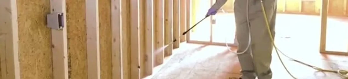 Termite treatment technician applying spray along framing and unfinished walls in Glendale, AZ