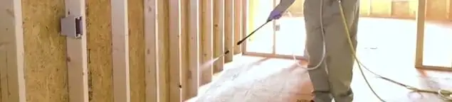 Termite treatment technician applying spray along framing and unfinished walls in Glendale, AZ