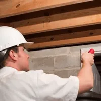 Termite inspection technician checking a basement wall and framing for termite activity in Glendale, AZ